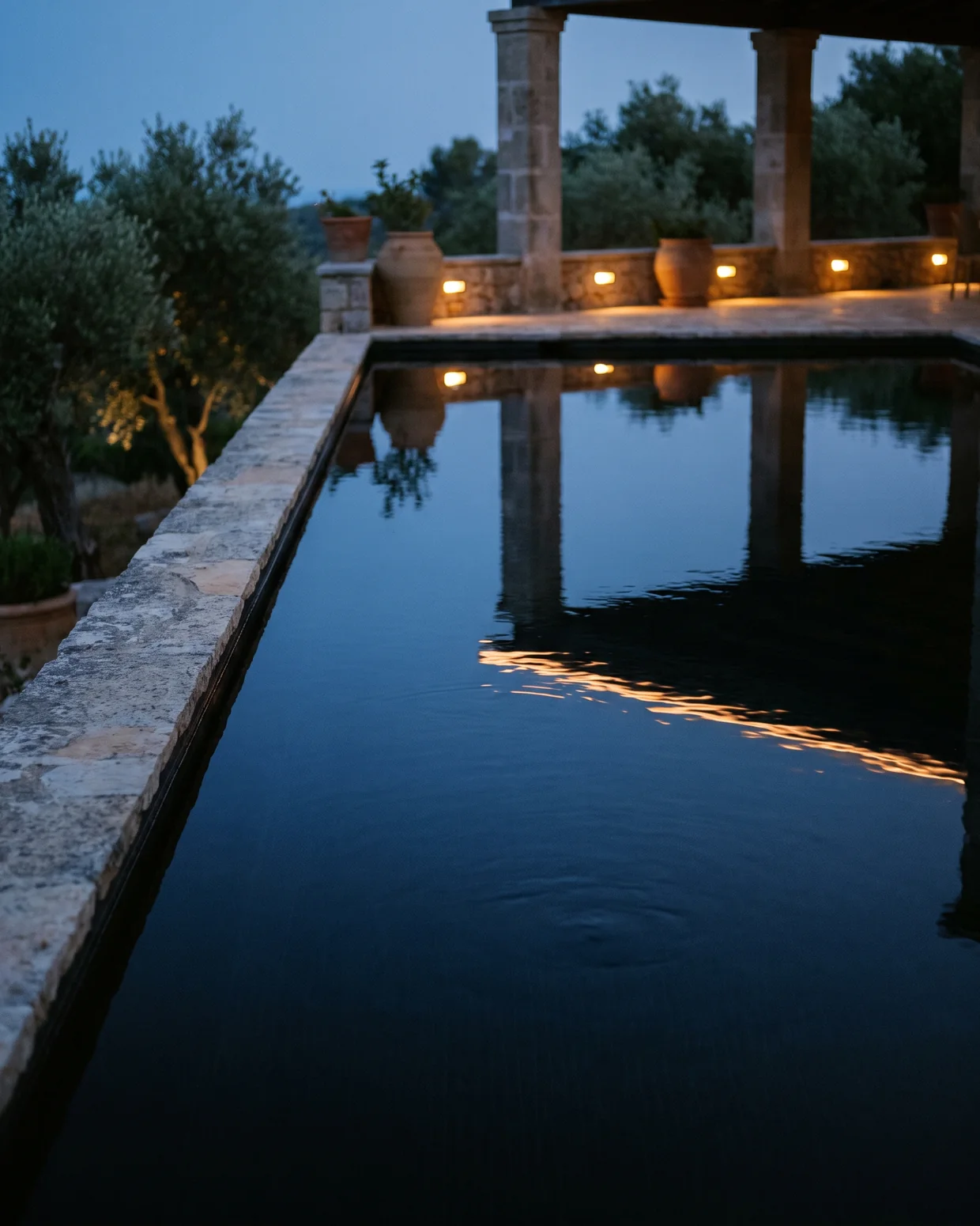 Dunkler, spiegelnder Pool einer mediterranen Villa zur blauen Stunde